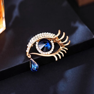 Golden eye-shaped brooch with blue crystal teardrop and sparkling rhinestones on black box