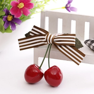 Cute cherry bow hair clip with glossy red cherries and brown striped ribbon on a white bench