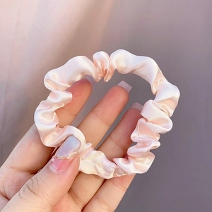 Handheld shot of a soft pink satin silk hair scrunchie with smooth pleated fabric texture