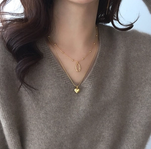 Close-up of double-layer gold heart necklace with geometric pendant on knit sweater