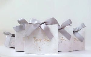 Detailed view of four marble pattern gift bags with grey ribbon bows and gold Thank You text