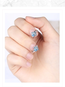 Macro view of blue zircon paw print earrings worn on fingers to show delicate scale