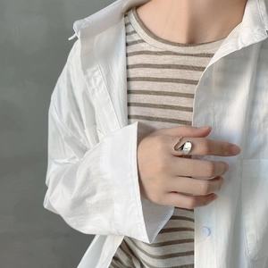 Close-up of irregular liquid metal style silver ring worn by a model in a minimal outfit
