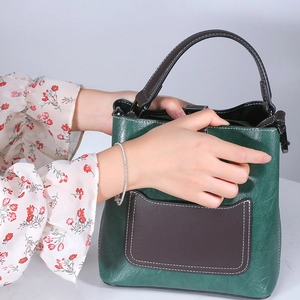 Minimalist green bucket bag in premium leather with a brown pocket and top handle