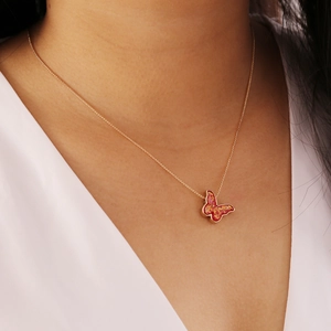 Detail einer roten Glitzer-Schmetterlingskette mit goldener Kette am Frauenmodell