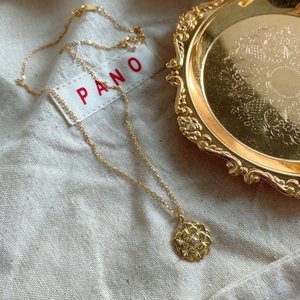 Macro detail of golden flower pendant with centered zircon on vintage metal tray