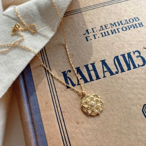 Detailed view of a gold rose petal pendant with a small zircon on a thin cross chain