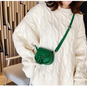 Girl wearing a mini green leather crossbody bag with tassel detail over a white sweater