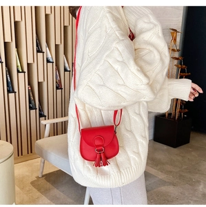Detail of a red mini crossbody bag with tassels shown on a model in a cozy knit sweater