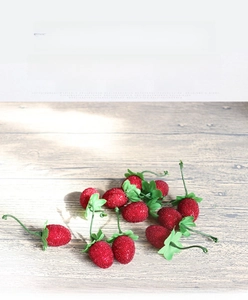 Detailed close-up of realistic artificial red strawberries with green leaves on wood