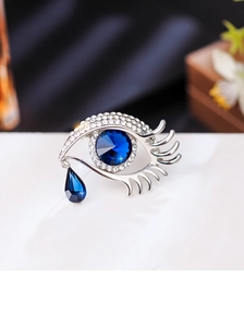 Macro detail of silver eye brooch featuring sparkling diamonds and blue crystal teardrop
