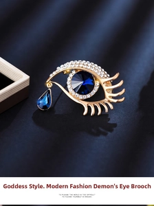 Macro detail of gold-plated evil eye brooch with blue crystals on blue satin background