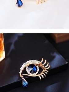 Macro shot of gold Evil Eye brooch with blue crystal and teardrop pendant on black background