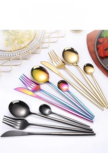 Polished gold and black stainless steel cutlery set arranged on a dining table setup