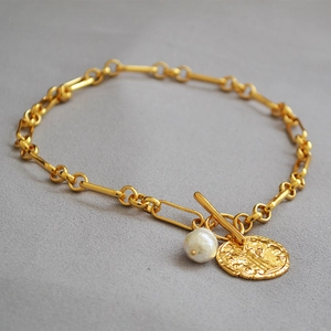 Detalle de pulsera de cadena dorada con perla barroca, moneda colgante y cierre de barra