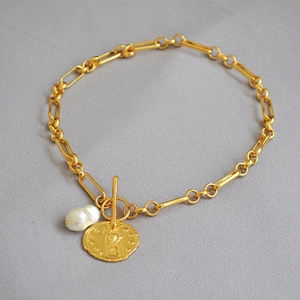 Detalle de pulsera de cadena dorada con perla barroca, moneda en relieve y cierre de tipo OT