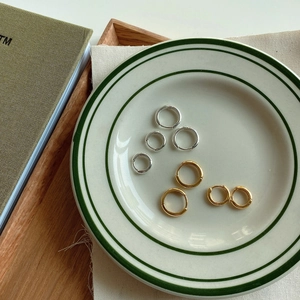 Three sizes of minimalist gold and silver hoop earrings on a vintage white porcelain plate