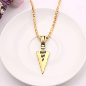 Detail of a carved golden arrowhead pendant on a woven chain over a ceramic plate