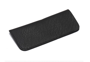 Gros plan sur la texture du cuir noir à motif litchi et les coutures de la pochette à lunettes