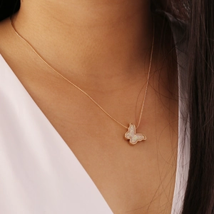 Minimalistische Goldkette mit weißem Opal-Schmetterlingsanhänger am Hals des Modells