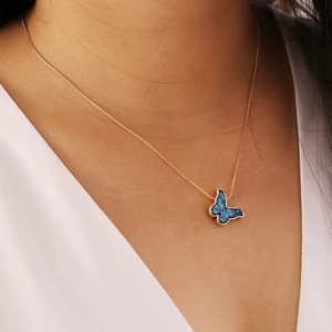 Nahaufnahme einer goldene Halskette mit blauem Opal-Schmetterlingsanhänger am Model