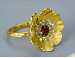 Macro shot of 925 silver flower ring with red garnet stone and matte gold finish