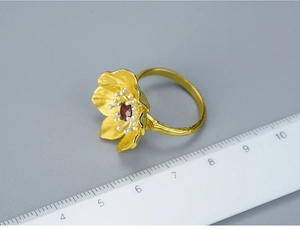 Macro shot of gold floral ring with red gemstone and ruler for size measurement