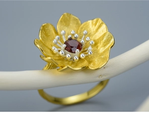 Macro detail of a golden flower ring with a red garnet stone and silver stamen accents