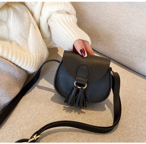 Detail of mini black PU leather saddle bag with tassel on soft fabric background