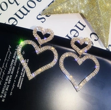 Dettaglio di orecchini a doppio cuore dorati con strass su supporto in carta nera