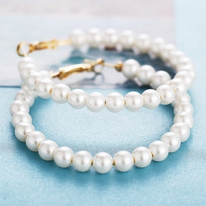 Elegant white pearl hoop earrings with gold-tone metal clasp on light blue background