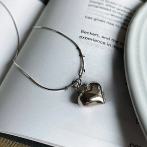 Close-up of minimalist silver heart pendant with octagon snake chain on book background