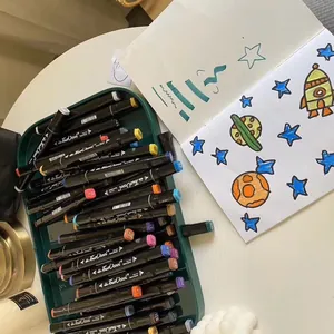 Close-up of dual-tip sketch markers in a storage tray beside a colorful drawing book