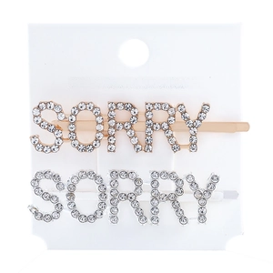 Detail of gold and silver SORRY metal hair clips with rhinestones on white card