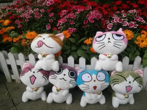 Detailed close-up of six plush cats with colorful spots and golden bells in a garden
