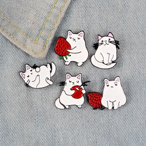Détail de cinq broches chat en émail blanc avec fraises rouges sur tissu en jean bleu