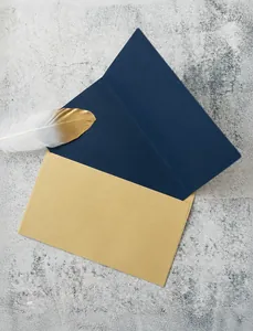 Detail view of navy card and kraft envelope with golden feather decor on stone background