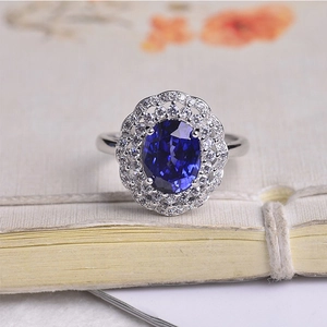 Close-up of silver ring featuring oval deep blue sapphire and double diamond halo