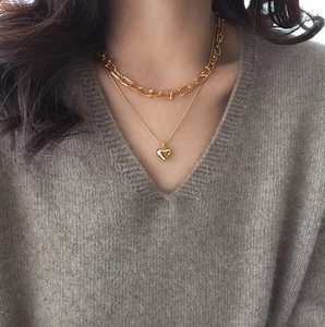Detailed view of layered gold heart necklace and horseshoe link chain on model neck