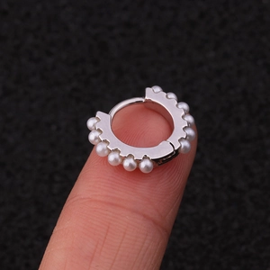 Silver circular ear cuff with white pearls shown on finger with black background