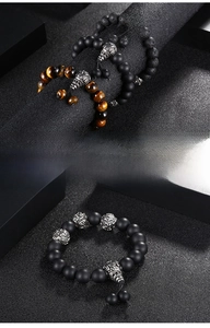 Detail of men's beaded bracelets featuring tiger eye, lava stone, and steel charms