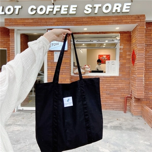 Detail of a black canvas tote bag with white tag shown in a street lifestyle setting