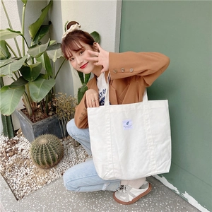 Detail of off-white corduroy tote bag with woven label shown in a lifestyle setting