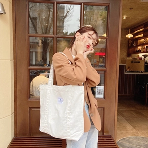 Minimalist white canvas tote bag shown worn over the shoulder in a casual lifestyle setting