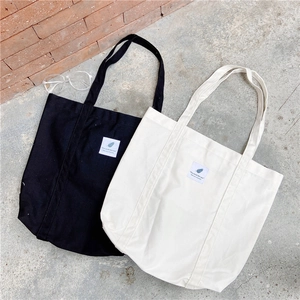 Close-up of black and cream canvas tote bags with 'You need this one' label on a tile floor