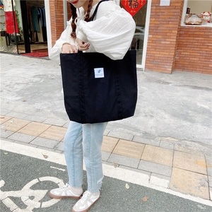 Street style view of a large black canvas tote bag carried by a model against brick wall