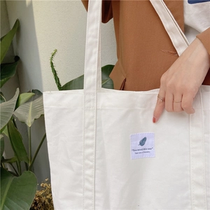 Detail of white canvas tote bag with decorative English label held by a model