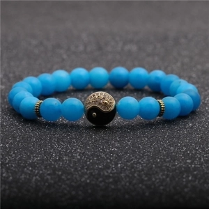 8mm blue agate bead bracelet with a gold and black Tai Chi Yin Yang charm on black background