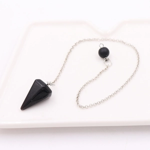 Macro shot of black crystal pendulum pendant with silver chain on white ceramic tray