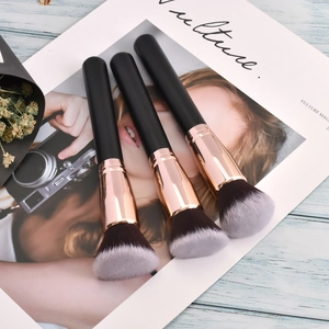 Three professional makeup brushes with rose gold ferrules on a stylish magazine background